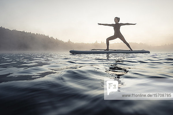 Frau praktiziert morgens Paddelbrett-Yoga auf dem Kirchsee  Bad Tölz  Bayern  Deutschland