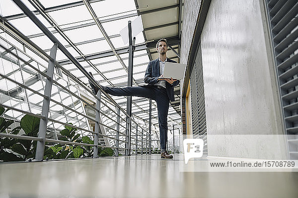 Auf einem Bein stehender Geschäftsmann in modernem Bürogebäude mit Laptop