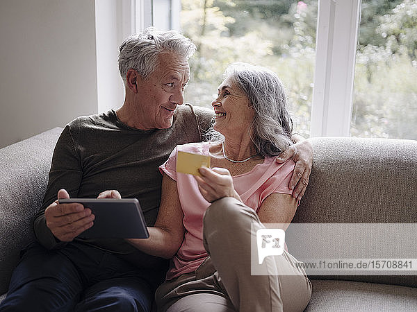 Glückliches älteres Ehepaar entspannt sich zu Hause auf der Couch und nutzt Tablet zum Online-Shopping