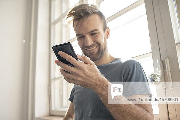 Lächelnder Mann mit Smartphone am Fenster