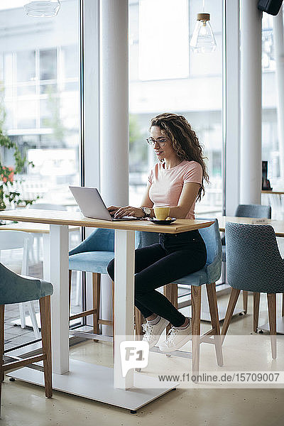 Junge Studentin arbeitet im Café an ihrem Laptop