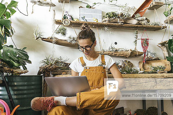 Junge Frau mit Laptop in einem kleinen Gartenbaubetrieb