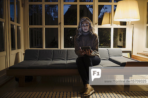 Reife Frau benutzt Tablette auf der Couch zu Hause im Dunkeln