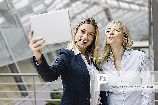 Zwei glückliche junge Geschäftsfrauen benutzen ein Tablett im Büro