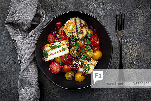 Schale mit persischem Salat mit Tomaten  gegrilltem Halloumi-Käse  Auberginen  Granatapfelkernen  Sumach  schwarzem Sesam und Petersilie