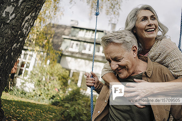 Glückliche Frau umarmt älteren Mann auf einer Schaukel im Garten