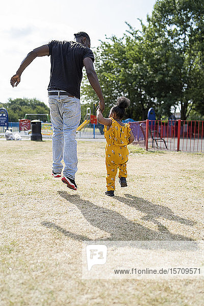 Rückansicht eines Vaters und einer Tochter  die Hand in Hand in einem Park spazieren