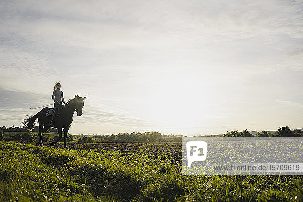 Frau reitet bei Sonnenuntergang auf einem Feld auf dem Land