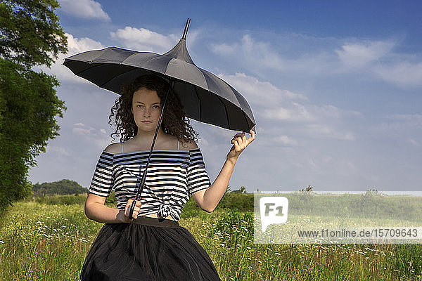 Porträt einer jungen Frau mit Regenschirm auf einer Wiese