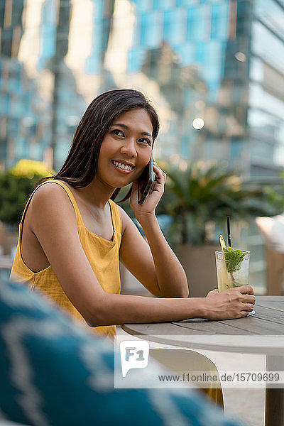 Porträt einer lächelnden Frau am Telefon  die mit einem Getränk in einem Cafe sitzt