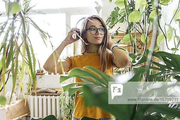 Young woman surrounded by plants listening to music with headphones