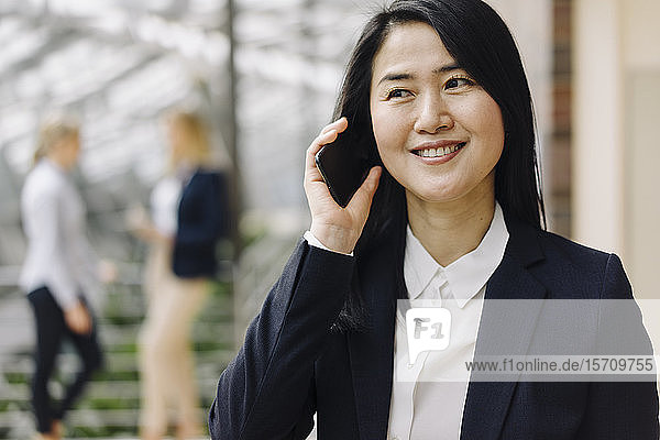 Portrait of a smiling businesswoman on the phone in office with colleagues in background