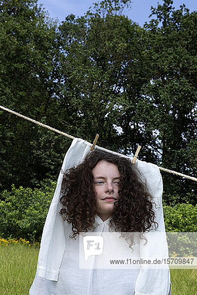 Bildnis einer jungen Frau mit braunen Locken in weißem Kleid  das auf der Wäscheleine trocknet