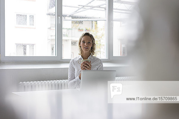 Porträt einer jungen Geschäftsfrau mit Laptop und Kaffeetasse am Schreibtisch im Büro