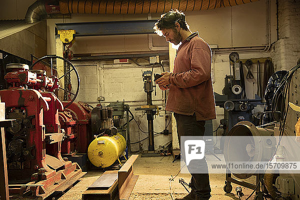 Metallarbeiter  der in der Werkstatt arbeitet  mit Smartphone