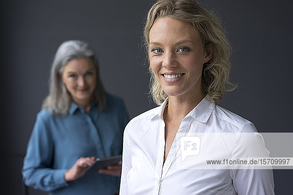 Porträt einer lächelnden jungen Geschäftsfrau mit einer reifen Geschäftsfrau im Hintergrund