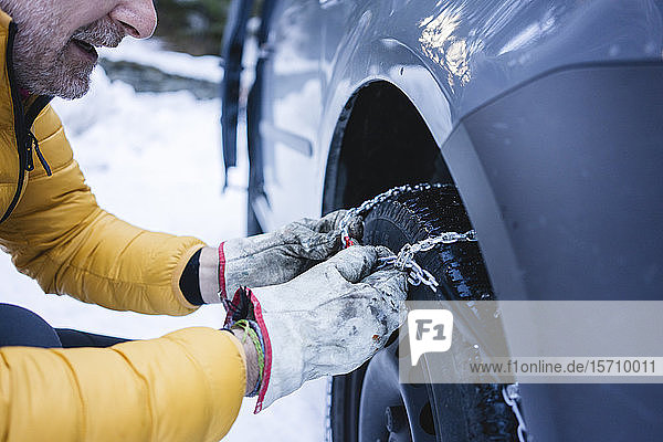 Mann legt die Schneeketten an sein Auto