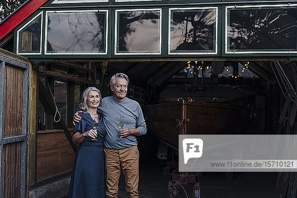 Älteres Ehepaar steht mit einem Glas Champagner vor dem Bootshaus