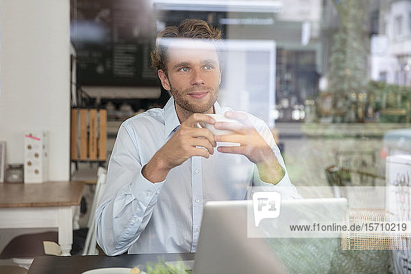 Junger Geschäftsmann mit Kaffeetasse und Laptop in einem Cafe