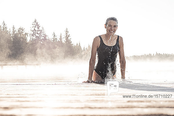 Glückliche Frau im schwarzen Badeanzug badet im Morgennebel in einem See