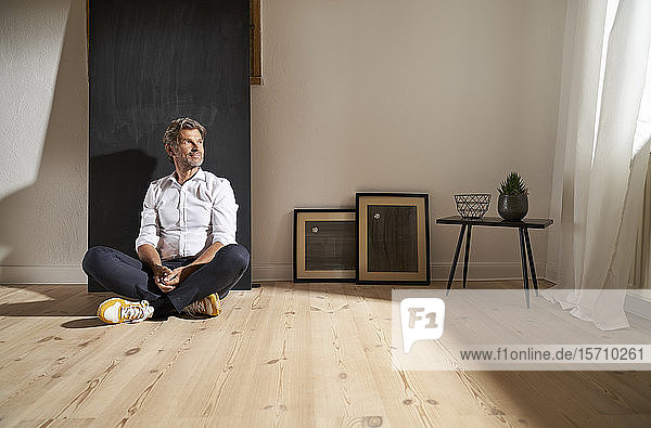 Porträt eines entspannten reifen Mannes  der zu Hause auf dem Boden sitzt und in die Ferne schaut