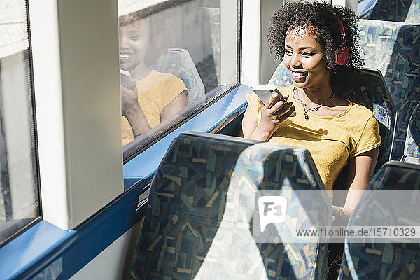 Lächelnde junge Frau mit Kopfhörern und Smartphone in einem Zug