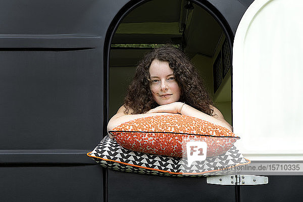Porträt einer auf Kissen gelehnten jungen Frau  die aus dem Wohnwagen schaut