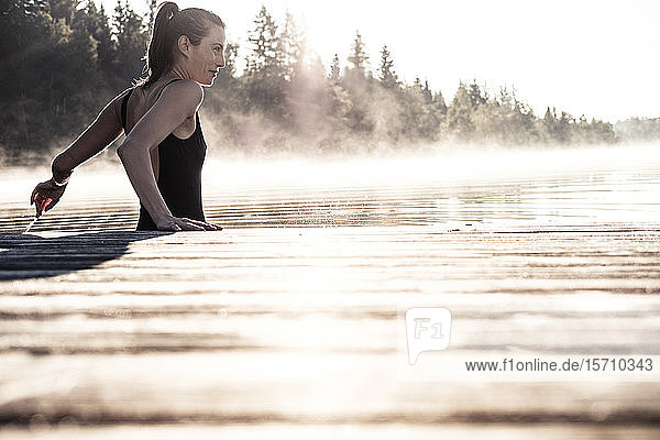 Frau im schwarzen Badeanzug badet im Morgennebel in einem See