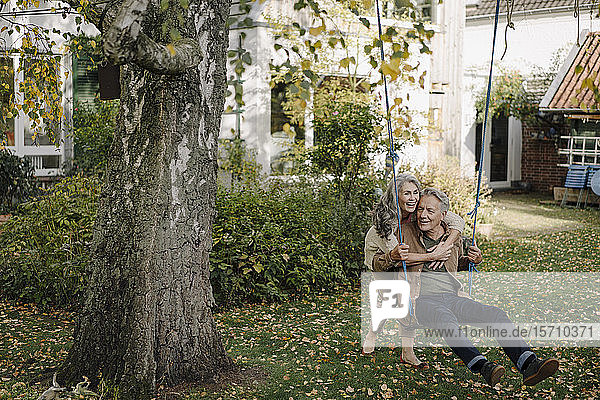 Happy woman embracing senior man on a swing in garden