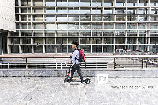 Junger Mann geht mit einem E-Scooter in der Stadt