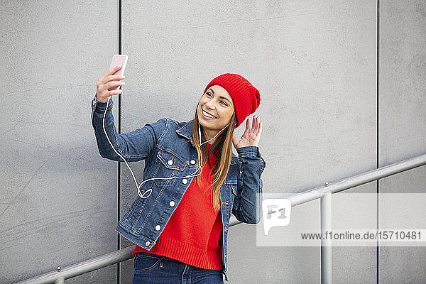 Frau mit rotem Pullover und Wollmütze  die sich ein Selfie nimmt