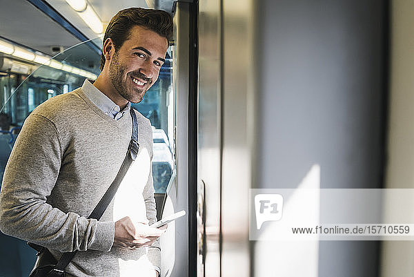 Porträt eines lächelnden jungen Mannes mit Smartphone in einem Zug
