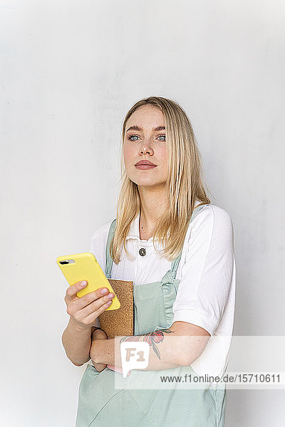 Porträt einer jungen Frau mit Notebook und Handy in der Hand