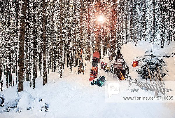 Österreich,  Salzburg,  Altenmarkt im Pongau,  Wintersportgeräte liegen bei Sonnenuntergang vor verschneiter Waldhütte
