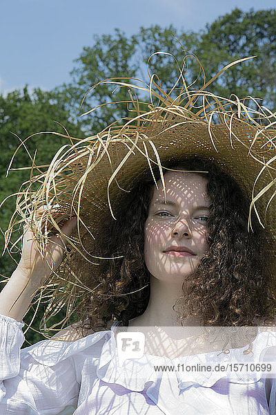 Porträt einer jungen Frau mit ausgefranstem Strohhut in der Natur