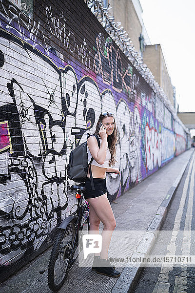 Lächelnde junge Frau am Telefon an Graffiti-Wand