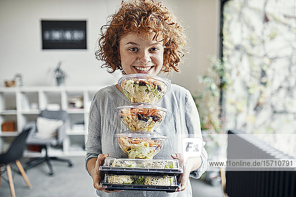 Porträt einer lächelnden Geschäftsfrau  die einen Stapel Essen zum Mitnehmen im Büro hält