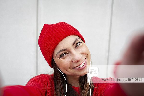 Frau mit rotem Pullover und Wollmütze vor einer Wand