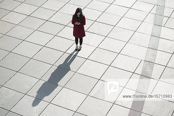 Geschäftsfrau benutzt Smartphone und steht auf Betonboden