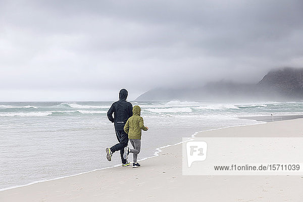 Backview of father and daughter jogging on the beach  Nordhoek  Western Cape  South Africa