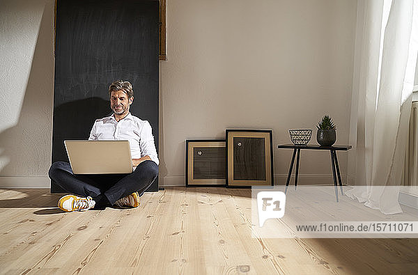 Entspannter reifer Mann sitzt zu Hause mit Laptop auf dem Boden
