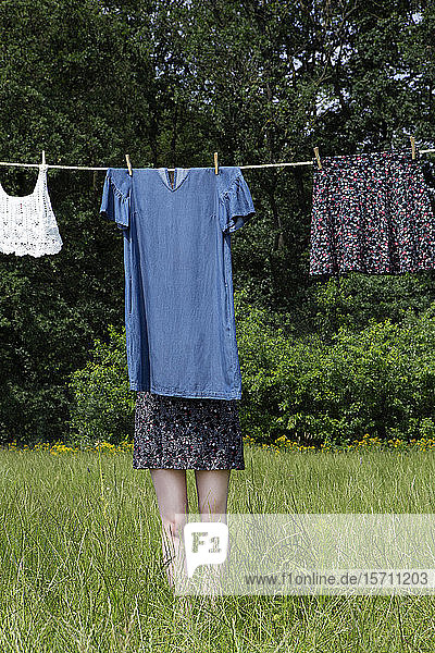 Junge Frau versteckt sich hinter einem auf der Wäscheleine trocknenden Kleid
