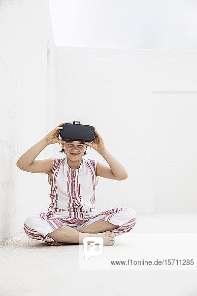 Girl with VR goggles sitting on ground of empty space