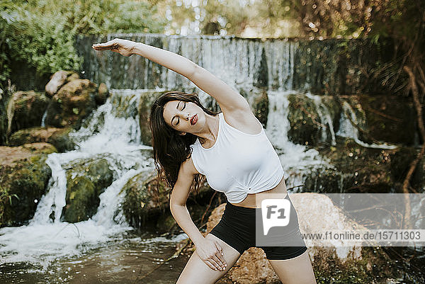Junge Frau praktiziert Yoga auf einem Wasserfall