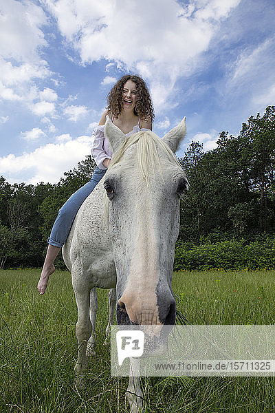 Porträt eines grasenden Pferdes mit lachendem Reiter auf dem Rücken