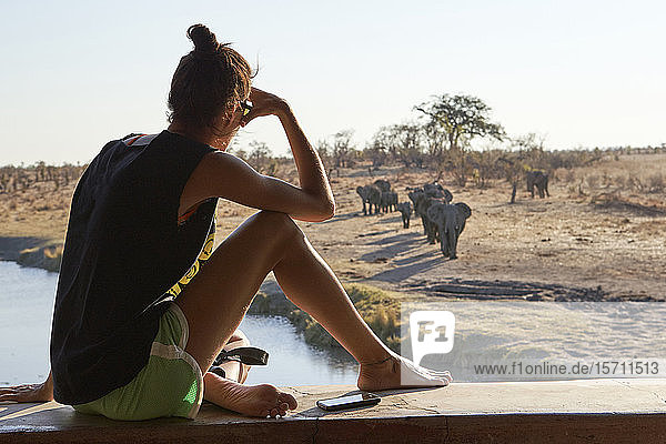 Frau beobachtet eine Elefantenherde im Fluss von einem Aussichtspunkt aus  Hwange-Nationalpark  Simbabwe