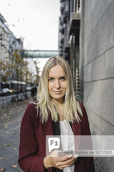 Blonde Geschäftsfrau mit Smartphone im Hintergrund moderne Gebäude