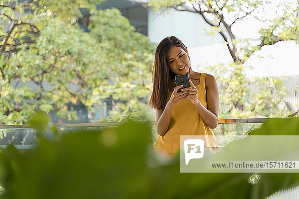 Porträt einer lächelnden  gelb gekleideten Frau mit Smartphone auf der Terrasse