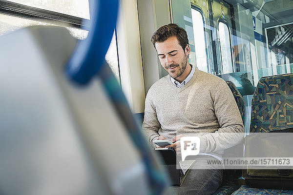 Junger Mann benutzt Smartphone und Tablet in einem Zug