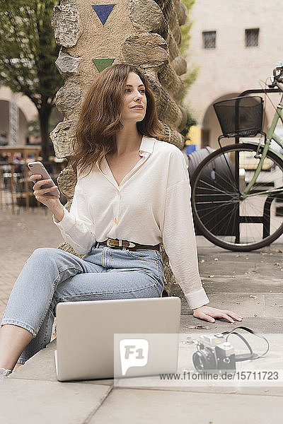 Junge Frau mit Smartphone  Kamera und Laptop im Freien